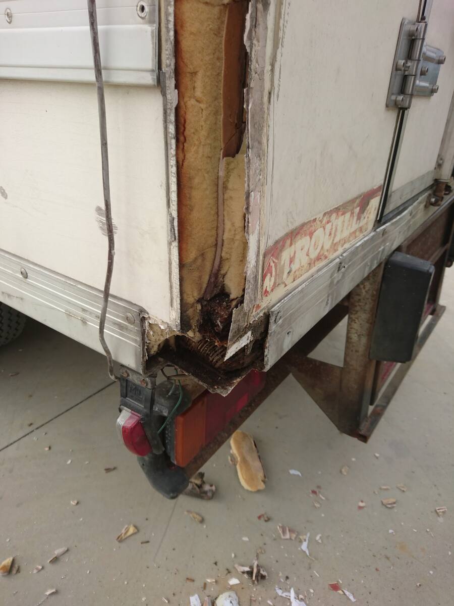 Angle arrière d'une caisse de fourgon arraché, bois et isolant à nu