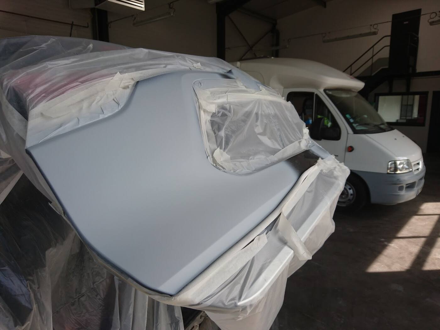 Zone réparée passée à l'apprêt gris, le reste de la voiture protégé sous un film de masquage